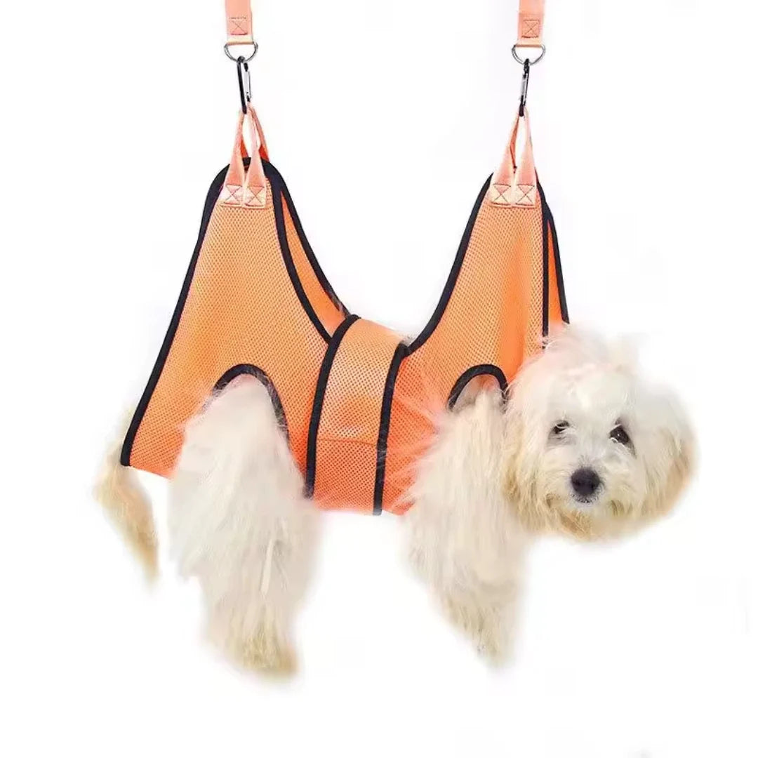 A small white fluffy dog secured inside an orange Petifo grooming hammock hanging against a white background.